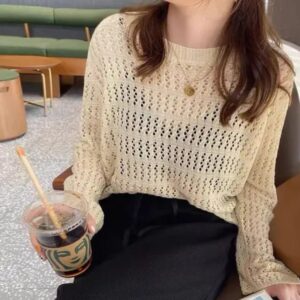 Woman wearing a cream crochet knit long sleeve sweater with an open-knit design