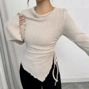 Woman wearing a cream ribbed long sleeve top with adjustable side ruching and an asymmetrical hem
